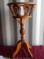 Front view of vintage wooden plant stand showing circular top with cutout designs in the wood and central turned column.