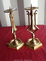 Pair of brass nautical candlesticks standing upright on red background, showing full height and design details including the round candle plate with spike and mounting base.