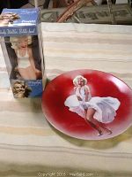 Photo showing both the Marilyn Monroe collector plate and the boxed Funko bobble-head on a striped fabric surface.