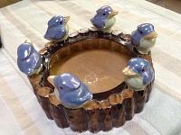 Top and angled side view of a round porcelain dish styled like a tree stump with six detailed, blue and white birds perched evenly around the circular edge.