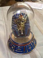 Full view of the Mask of Tutankhamen figurine encased in clear glass dome on a decorated base