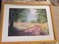 Frontal image of the watercolour painting showing a dirt path meandering through a wooded area, framed with a light wooden frame and white matting.