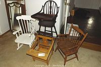Four vintage children's chairs grouped on carpeted floor including white rocker, stained wood high chair, teak chair, and wooden potty chair.