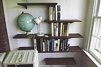 Wide view showing six solid teak wall-mounted shelves holding a collection of hardcover books, a globe, and two small lamps.