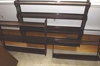 Full view of three mahogany wall mounted shelves arranged on floor against wall, showing carved sides and various shelf sizes.