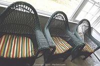 Three green painted wicker armchairs with striped cushions positioned indoors near windows.