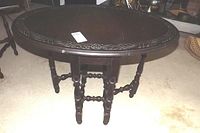 Oval carved wooden table with drop leaves and detailed carved border on the tabletop, shown fully closed.