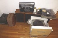 Overview photo showing the Technics turntable with dust cover, two Realistic speakers, Hitachi portable stereo system above speakers, and cases for projectors.