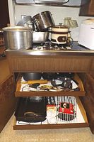 Photo of pots, pans, Rival slow cooker crock pot, and some kitchen utensils on stove and in lower drawer