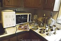 Photo showing Breadman Plus bread maker, Sanyo microwave oven, Swiss Harmony music decanter, and several metal cups on kitchen counter.