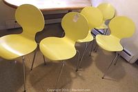 Photo showing five yellow Jacobsen style side chairs grouped together with their distinctive bentwood molded seat and backrests and chrome tubular legs, placed near a wooden table.