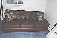 Full view of the brown leather couch with three seat cushions and two striped throw pillows placed on each side, against a light wall and blue carpet.