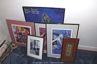 All six framed artworks arranged leaning against the wall showing variety in frame colors and art styles.