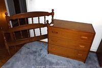 Full view of twin wooden headboard and footboard alongside teak veneer three drawer dresser on carpeted floor.