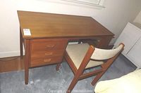 Front view of wooden desk with three drawers closed, locked upper drawer, and coordinating chair with padded seat and back.