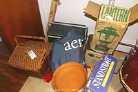 Photo of camping gear including boxed Coleman Floodlight Green Lantern, green cooler, woven picnic basket, Aero Extra bed roll, and various boxed items.