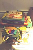 Stack of various vintage board games including Jeopardy and Foto Electric Football with game boxes showing wear.