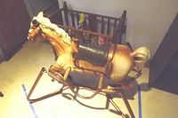 Photo showing the vintage spring rocking horse with visible wear and a wooden toy crib in the background.