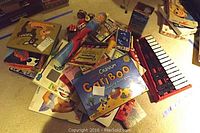 Pile of children's games and toys laid on floor including Cranium Cariboo, puzzles, toy phone, and backgammon box