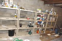 Four beige plastic shelving racks against a cinder block wall, loaded with various household and garage items like paint cans and boxes.