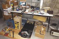 Wide view showing folding table with assorted tools on and around it, boxes present underneath and beside, including circular saw, hand tools, and levels.