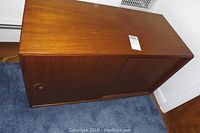 Front angle view of cabinet closed showing wood finish and sliding doors with recessed round handles.