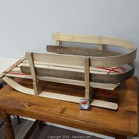 Side view of wooden Torpedo brand sleigh showing curved runners, slatted seat, and red pull rope on wooden table.