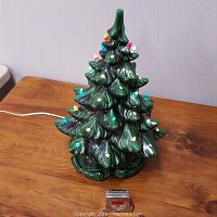 Full view of the green ceramic Christmas tree with colored bulbs, lit and plugged in on a wooden surface