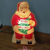 Front view of light up plastic Santa Claus decoration showing 'Merry Christmas' banner with Christmas tree design.