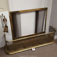 Fireplace surround, mesh screen, and part of fireplace tools visible, arranged against wall on carpeted floor