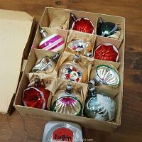 Boxes of 11 antique Christmas bulbs made of glass, showing various colors including silver, red, green, pink, and purple with cratered reflective centers and painted decoration.