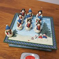 View of Tic Tac Toe board with snowmen playing pieces set inside board grid positions, depicting winter scene with snow and trees on the square wooden board