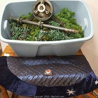 Plastic storage bin filled with artificial evergreen tree branches, poles, and metal base. Ice blue tree skirt is draped beneath the bin, featuring a quilted shiny texture and embroidered snowflakes.