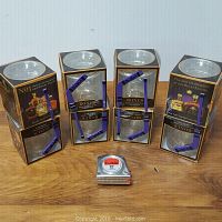 Four boxed Crown Royal limited edition glasses each paired with a bonus hockey stick shaped stir stick sitting on a wooden surface, accompanied by a 12-foot tape measure for scale.