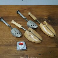 Top view of two pairs of shoe stretchers, one metal and wood, one fully wooden, displayed on a wooden surface along with a Lufkin measuring tape as size reference.