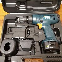 Photo showing Black & Decker 9.6V cordless drill in blue and black with orange trigger inside black molded plastic carrying case. Battery and charger also visible.