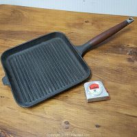 Full view of square cast iron grill skillet with wooden handle and measuring tape for scale placed beside it.