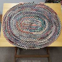 Full top view of oval patchwork braided rug placed on a wooden table, showing its size and multicolor pattern.