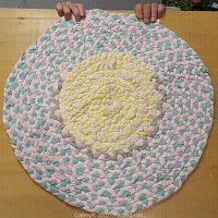 Top-down view of the 25 inch braided rag rug showing pastel colors and braided texture on a wooden table.
