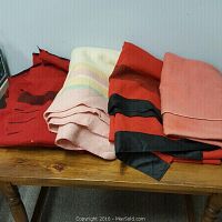 Four wool blankets folded on a wooden surface, showing different colors and some damage like rips and stains.