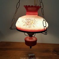 Photo showing the full hanging lamp lit, highlighting the floral design on the glass shade and red ruffled top.