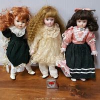 Front view of three porcelain-faced dolls standing together showing their clothing and hair styles.