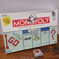 Front view of the Monopoly game box wrapped in plastic with Monopoly logo and game property squares visible.