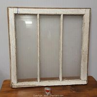 Front view of the vintage three pane wooden window showing the white painted frame and glass panes, with the middle pane broken.