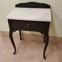 Front view of a small black wooden entryway table with an unpolished smooth granite top and single drawer with a metal pull handle.