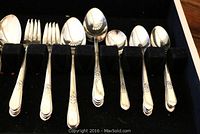 Close-up view of various silverplate flatware pieces, including spoons and forks, showing ornate floral handle design.