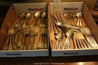 Two cardboard trays filled with assorted silverplate flatware including forks, spoons and knives of various patterns and ages.