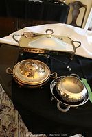 Set of silverplate items on black and white cloth background; includes chafing dish, round covered serving dish, rose bowl and round ring