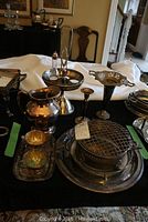 Table display of all silverplate items included in the lot showing candlesticks, various vases, jug, and flower frog on platters.