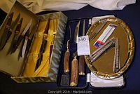 Two boxed carving sets including knives and forks with wooden handles, an oval brass-colored serving tray with two metal nutcrackers and two metal meat pullers.